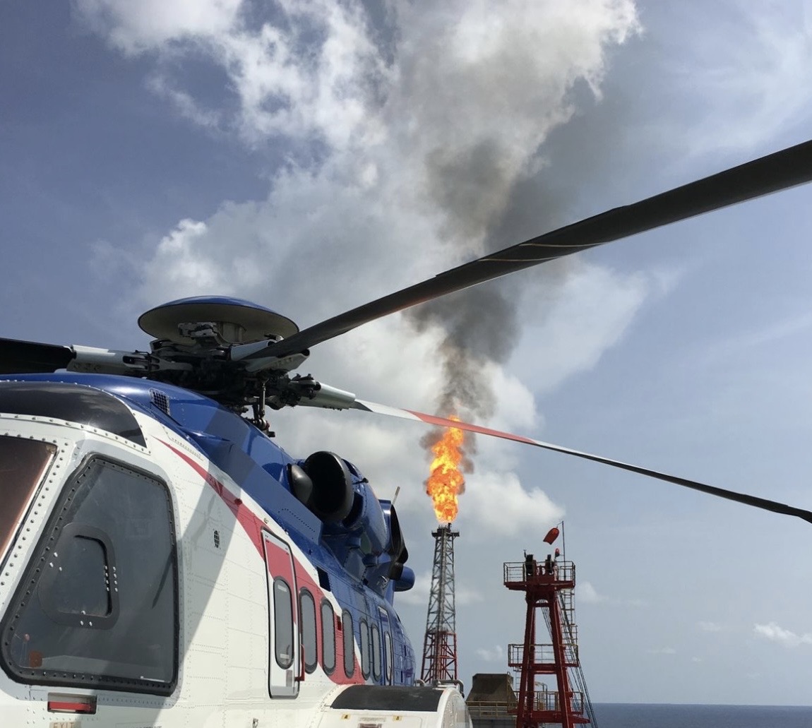 Helicopter on offshore platform helipad with gas flare stack